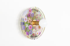 Modern two light wall sconce with brass hardware and purple flowers. Features resin-encapsulated orange flowers with greenery, ferns, and leaves.  Adds a real-like nature theme to any interior design project.  Called the Botanico Sconce by Sazerac Stitches. Features purple flowers with greenery