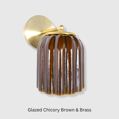 The Marcella Sconce pairs a richly glazed, fluted shade in chicory brown with a simple brass arm and backplate, giving it real texture without needing a busy silhouette to stand out. The ribbed, scalloped-edge shade catches light differently from every angle, making it a strong choice for a bathroom vanity, powder room, or entryway that wants a warm, tactile fixture instead of a plain glass shade.