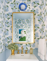 Grandmillennial bathroom decor featuring hydrangea chinoiserie wallpaper, pale blue wainscoting, brass faucet and mirror, plus a sky blue ceramic leafy sconce with white globe light.