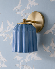 White birds scatter mid-flight across this sky blue wallpaper, and the Marcella Sconce in Sky Blue matches the ground so closely it nearly vanishes into the scene, leaving the brass hardware and fluted texture to give it away. A tonal, whimsical pairing for coastal traditional bathrooms and powder rooms that want a sense of movement and sky built right into the walls.