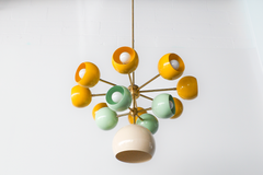 Closeup of the Solaris chandelier featuring a sculptural brass frame with rounded globe shades in bright yellow and mint green, each orb shade open at the front to spotlight the white bulb, paired with a cream downlight shade, perfect for playful modern interiors, Palm Springs inspired mid century decor, and maximalist homes where lighting is treated like functional art.