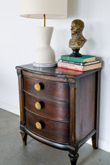 Dark Nightstand with a modern cream lamp by Sazerac Stitches and brass sun-shaped cast brass drawer pulls.  Antique books and a vintage bust of Napoleon.