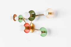 Taurus wall fixture in earthy tones with brass arms, featuring brown, mint, olive, cream, and terracotta circular discs with globe bulbs. A sculptural constellation-inspired light for eclectic, organic modern, and color-forward interiors.