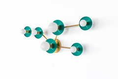 Studio product photo of the Taurus constellation wall sconce by Sazerac Stitches, shown in Mermaid Green powder-coated steel discs with warm brass arms. The sculptural star-map layout uses two larger circular discs with larger frosted globe bulbs and three smaller star discs with smaller globe bulbs, creating a modern graphic constellation pattern. Clean white background with generous negative space, ideal for searches like green wall sconce, emerald or teal bathroom lighting, brass and green sconce, mid ce