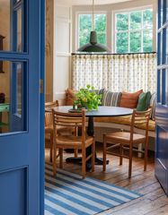 Bruxelles Pendant Light in olive green with brass stem, hanging in a traditional breakfast nook with built-in banquette seating, round dining table, striped blue rug, and wooden chairs. Bright cottage-style kitchen nook with layered pillows, white paneled walls, floral curtains, and large windows. Custom handmade pendant lighting by Sazerac Stitches, perfect for breakfast nooks, dining spaces, and cozy kitchen corners.