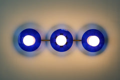 Bright Blue Triple Circus Sconce: Bold and dazzling, the Bright Blue Triple Circus Sconce captures the essence of Murano glass with its vibrant blue acrylic disc. Each intricately etched disc casts mesmerizing light and shadow patterns, transforming your walls into a captivating display.