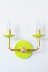 This two-arm candle sconce swaps the expected neutral finish for a bold chartreuse, with scalloped bobeche cups beneath frosted flame-tip bulbs and classic curved brass arms. It is the kind of colorful, powder-coated lighting that reads maximalist and anti-beige rather than builder-grade, good for a hallway, dining room, or powder room that wants a little more nerve.