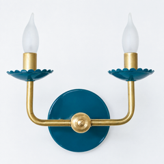 A classic, traditional style two-arm candle sconce takes on a soft, dusty teal-blue here, with scalloped bobeche cups beneath frosted flame-tip bulbs and traditional curved brass arms. It reads more tonal and coastal than a bright blue, a good fit for a room leaning quietly colorful rather than bold. Lagoon and brass wall sconce.