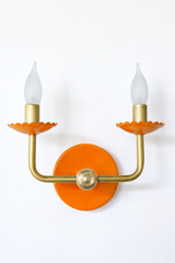 A classic two-arm candle sconce gets a color update here, with scalloped bobeche cups in a warm orange beneath frosted flame-tip bulbs and curved brass arms. It is the kind of powder-coated lighting that trades safe and neutral for a little personality, well suited to a colorful traditional dining room or hallway.