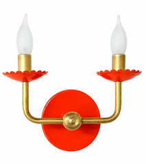 This two-light sconce is a great pick for a bathroom or hallway that wants a jolt of color without losing its shape. The curved brass arms have a clean, almost Scandinavian modern line, while the scalloped bobeche cups and candelabra-style bulbs above them are a classic, old-world detail. It's mounted in a raw, unlacquered brass that keeps things warm and traditional even as the bright red-orange powder coat does something bolder and more playful. That contrast, a simple modern silhouette wearing a traditio