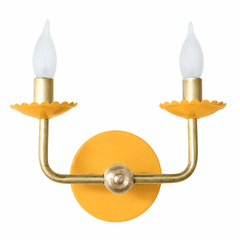 A warm mustard yellow wall sconce that brings sunshine to a breakfast nook, kitchen, or cheerful bathroom. The Two-Light Adele pairs a golden powder-coated finish with warm brass arms and a scalloped, flower-shaped bobeche under each candle. It has an English cottage warmth to it, the kind of happy color that plays well with florals, gingham, and old-house millwork. Available in a range of powder-coated colors for rooms that skip the beige.
