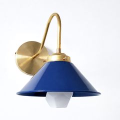 A navy cone catches the light in a small bathroom, over a pedestal sink, pairing unexpected color with a gooseneck brass arm that reads both traditional and industrial. The clean geometry works equally well in a powder room, a kitchen breakfast nook, or flanking a kid's bedroom mirror—this is the sconce that adapts to wherever personality lives. Swap the navy for any Sazerac Stitches color to echo wallpaper, accent tile, or a collected moment on the wall.