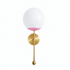 A sweet globe sconce for a powder room, girl's room, or bedside that wants a wall light with a little romance. The Verbena Sconce sets a round brass backplate with a slim brass stem, seats a white glass globe in a soft blush-pink cup, and finishes the bottom with a small brass ball, the kind of detail that makes it feel custom. Blush and brass together read grandmillennial and gently feminine without going saccharine, lovely flanking a mirror, art, or a bed. A soft, glowing light for romantic, mid-century, 