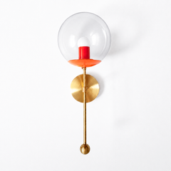 A rich jewel-tone clear-globe sconce for a powder room, bedside, or hallway that wants a wall light with a genuinely custom feel. This Verbena Sconce swaps the usual opaque shade for a clear glass globe, so the bulb shows through, seated in an orchid-purple cup with a deep black-cherry socket sleeve inside for a saturated two-tone pairing. A slim brass stem, round backplate, and small brass ball finish it below. The purple-and-berry combination reads bold and a little sultry, the kind of considered detail t
