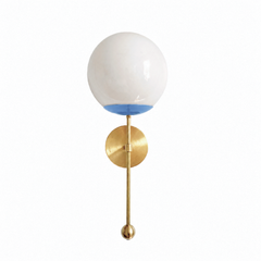 A soft periwinkle globe sconce for a powder room, bedside, or hallway that wants a wall light with gentle, airy color. The Verbena Sconce tops a round brass backplate with a slim brass stem, seats a white glass globe in a hydrangea-blue cup, and finishes the bottom with a small brass ball, the kind of detail that makes it feel custom. This dusty periwinkle and brass together read sweet and a little Southern, lovely flanking a mirror, art, or a bed, especially in a coastal or grandmillennial space. A soft, g