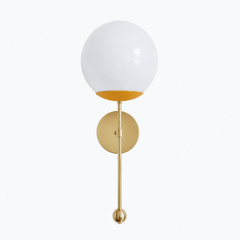A warm mustard globe sconce for a powder room, bedside, or breakfast nook that wants a wall light with sunny, vintage-cheerful color. The Verbena Sconce tops a round brass backplate with a slim brass stem, seats a white glass globe in a soft matte golden-yellow cup, and finishes the bottom with a small brass ball, the kind of detail that makes it feel custom. Mustard and brass together read warm and a little retro, riding the butter-and-golden trend while feeling timeless, lovely flanking a mirror, art, or 