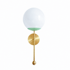A soft mint globe sconce for a powder room, nursery, or bedside that wants a wall light with fresh, airy color. The Verbena Sconce tops a round brass backplate with a slim brass stem, seats a white glass globe in a pale mint-green cup, and finishes the bottom with a small brass ball, the kind of detail that makes it feel custom. Mint and brass together read gentle and spa-fresh, lovely flanking a mirror, art, or a bed, especially against white trim, wallpaper, or natural wood. A soft, glowing light for mid-