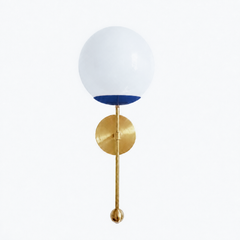 A rich navy globe sconce for a powder room, bedside, or hallway that wants a wall light with classic, easy-to-live-with color. The Verbena Sconce tops a round brass backplate with a slim brass stem, seats a white glass globe in a deep navy cup, and finishes the bottom with a small brass ball, the kind of detail that makes it feel custom. Navy and brass together read timeless and confident, at home flanking a mirror, art, or a bed, especially in a coastal or traditional space. A soft, glowing light for mid-c