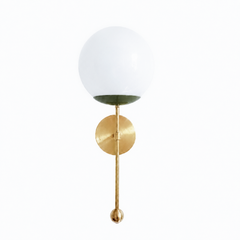 An earthy olive globe sconce for a powder room, study, or bedside that wants color with some backbone. The Verbena Sconce tops a round brass backplate with a slim brass stem, seats a white glass globe in a deep olive-green cup, and finishes the bottom with a small brass ball, the kind of detail that makes it feel custom. Olive and brass together read grown-up and a little vintage, lovely flanking a mirror, art, or a bed, especially against warm wood, dark walls, or collected antiques. A soft, glowing light 