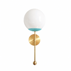A breezy poolside-aqua globe sconce for a powder room, bathroom, or kids' space that wants a wall light with happy, retro color. The Verbena Sconce tops a round brass backplate with a slim brass stem, seats a white glass globe in a light aqua cup, and finishes the bottom with a small brass ball, the kind of detail that makes it feel custom. Aqua and brass together read cheerful and a little Palm Springs, lovely flanking a mirror, art, or a bed, especially against white tile, rattan, or natural wood. A fresh