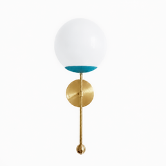 A soft dusty-teal globe sconce for a powder room, bedside, or hallway that wants a wall light with easy, coastal color. The Verbena Sconce tops a round brass backplate with a slim brass stem, seats a white glass globe in a blue-teal cup, and finishes the bottom with a small brass ball, the kind of detail that makes it feel custom. This gentle teal and brass together read fresh and a little coastal, lovely flanking a mirror, art, or a bed, especially against white trim, patterned tile, or natural wood. A sof
