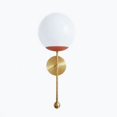 A warm terracotta globe sconce for a powder room, bedside, or hallway that wants a wall light with earthy, sun-baked color. The Verbena Sconce tops a round brass backplate with a slim brass stem, seats a white glass globe in a matte clay-toned cup, and finishes the bottom with a small brass ball, the kind of detail that makes it feel custom. Terracotta and brass together read grounded and organic, lovely flanking a mirror, art, or a bed, especially against white plaster, natural wood, or zellige tile. A sof