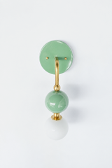 A statement wall sconce for rooms that want color with a calm, collected feel. This angle of the Ida sconce puts the bold round sage-green backplate front and center, with a brass arm curving down to a glossy green sphere and frosted glass globe. Soft, muted, and quietly confident, it's a soothing pick for colorful bathrooms, powder rooms, bedrooms, and eclectic spaces that want one gentle, standout detail.