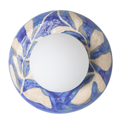 Handmade one-of-one watercolor blue and white leafy ceramic globe sconce with a matte white round globe shade mounted on a white wall, glossy botanical brushstroke pattern, sculptural artisan wall light for bedside lighting, hallway accent lighting, entryway statement, and bathroom vanity style spaces in modern, coastal, and grandmillennial decor