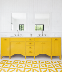 A double vanity in a saturated, confident yellow, paired with a graphic yellow-and-white geometric floor and crisp white subway tile. Brass and yellow double-ball knobs finish off every drawer and door, tying the hardware directly into the cabinetry color instead of playing it safe with chrome pulls. A strong reference for anyone building a bathroom with real commitment to color, not just a single accent.