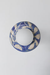 One-of-one handmade ceramic globe wall sconce lit on a wall with a warm halo of light, featuring a glossy blue and white watercolor leafy botanical pattern and a matte white globe shade, artisan statement lighting for cozy bedside ambiance, hallway mood lighting, entryway accent light, and design-forward interiors