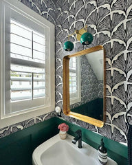 Colorful art deco inspired bathroom decor with graphic black and white patterned wallpaper, green wainscoting, and a two light green and brass wall sconce by Sazerac Stitches.