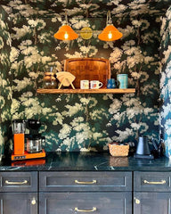 Colorful green botanical wallpaper with a bright orange wall sconce and dark cabinetry in a gorgeous coffee nook in a cabin