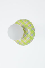 Angled studio view of a glossy plaid ceramic wall sconce in lime green, cream, and pale blue with a matte white globe shade, emphasizing the curved ceramic silhouette and reflective glaze, a colorful statement globe sconce for dopamine decor, eclectic modern interiors, playful wall lighting, and design-forward accent lighting in entryways, bedrooms, and powder rooms.