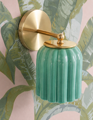 Large-scale banana leaves in layered green and sage cover this blush pink wallpaper, and the Marcella Sconce in Jade Green all but disappears into the pattern, its glossy fluted shade reading like part of the botanical illustration. Warm pink keeps the whole look inviting rather than jungly. Tropical traditional inspiration for bathrooms, powder rooms, and bedrooms that want pink and green with real depth.
