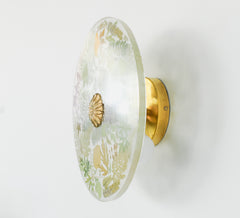 Botanical Wall Sconce with Brass Details – A decorative wall sconce featuring a round glass shade with embedded botanical patterns and a central brass accent, mounted on a brass base.