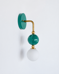 Rich, saturated vanity lighting that gives a bathroom or powder room real personality. Seen in profile, the Ida sconce shows off its curved brass arm reaching from a glossy teal-green backplate down to a stacked green sphere and frosted glass globe. The side view highlights the brass ball detailing and how the fixture projects off the wall. A jewel-toned, sophisticated choice for colorful traditional, grandmillennial, and coastal traditional interiors.