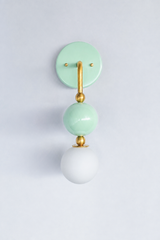 A statement wall sconce for rooms that want color with a soft, gentle feel. This angle of the Ida sconce puts the bold round pastel mint backplate front and center, with a brass arm curving down to a glossy mint sphere and frosted glass globe. Sweet, calming, and quietly pretty, it's a soothing pick for nurseries, girls' bedrooms, colorful bathrooms, and grandmillennial spaces that want one gentle, standout detail.