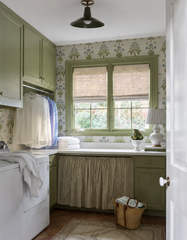 This laundry room treats a utility space like a real room, wrapping it in a cream, green, and blue botanical wallpaper and painting the cabinetry and window trim a deep olive green. The Bruxelles Flushmount overhead picks up the same green with clean chrome hardware, while a gathered fabric skirt, a ceramic lamp, and a woven market basket add the kind of personal touches that make even a laundry room feel considered.