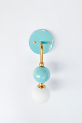 A soft aqua wall sconce for a nursery, boy's or girl's bedroom, or coastal powder room that wants fresh, breezy color. Shown straight on, the Ida sconce stacks a glossy pool-blue powder-coated sphere over a frosted glass globe, joined by warm brass hardware and a round aqua backplate. The head-on view shows how the spheres line up into a tidy vertical drop. Calm and cheerful, it's a standout for coastal traditional, grandmillennial, and playful kids' spaces.