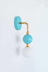 Fresh, breezy vanity lighting that gives a bathroom, powder room, or coastal bedroom a light point of view. Seen in profile, the Ida sconce shows off its curved brass arm reaching from a glossy pale aqua backplate down to a stacked blue sphere and frosted glass globe. The side view highlights the brass ball detailing and how far the fixture projects off the wall. An airy, soothing choice for coastal traditional, grandmillennial, and Southern traditional interiors.