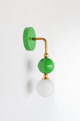 A glossy grass-green wall sconce for a bathroom, powder room, or entryway that leads with fresh, happy color. The Ida sconce stacks a saturated green powder-coated sphere over a frosted glass globe, joined by warm brass hardware and a round green backplate. Bright, garden-inspired, and cheerful, it's a standout for eclectic, English garden, and colorful traditional homes that skip the safe answer.