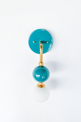 A rich turquoise wall sconce for a bathroom, powder room, or coastal bedroom that leads with saturated color. Seen in profile, the Ida sconce pairs a glossy teal powder-coated sphere with a frosted glass globe, joined by warm brass hardware and a round teal backplate. Watery, cheerful, and confident, it's a standout for coastal traditional, grandmillennial, Chinoiserie, and colorful traditional homes that skip the safe answer.