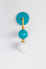 Rich, cheerful vanity lighting that gives a bathroom, powder room, or coastal bedroom a saturated point of view. Seen in profile, the Ida sconce shows off its curved brass arm reaching from a glossy turquoise backplate down to a stacked teal sphere and frosted glass globe. The side view highlights the brass ball detailing and how far the fixture projects off the wall. A happy, jewel-toned choice for coastal traditional, colorful traditional, and grandmillennial interiors.