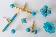 Collection of teal and brass cabinet hardware including a long double-ball cross-bar pull, a bar pull, a small double gumball knob, a single ball knob, a multi-ball cluster knob, and a scalloped flower knob, versatile colorful options for furniture makeovers, bathrooms, built-in cabinets, kitchens, kids' rooms, and offices.