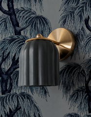 Ink-drawn weeping trees stretch across this blue-gray wallpaper, giving the wall a gothic, storybook mood. The Marcella Sconce in unglazed black plays it cool against all that illustration, its matte fluted shade letting the brass ball finial and ring collar be the only shine in the room. A striking pick for moody bedrooms, dark botanical powder rooms, and anyone drawn to wallpaper with real atmosphere.