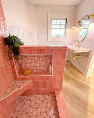 Large bathroom with pink tile shower, brass and porcelain vanity sink, and pink and brass wall sconces by sazerac stitches
