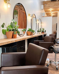 Modern Salon decorated with brass sconces by Sazerac stitches, wood and black features, and lots of potted plants