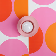 light pink wall sconce or ceiling light fixture on a retro orange and pink wallpaper design - front view