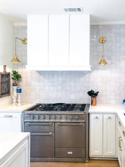 White kitchen with brass wall sconces on either side of the range top and oven.  Adds task lighting to a smaller kitchen