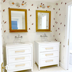 White double vanity bathroom with bird wallpaper and chrome sconces